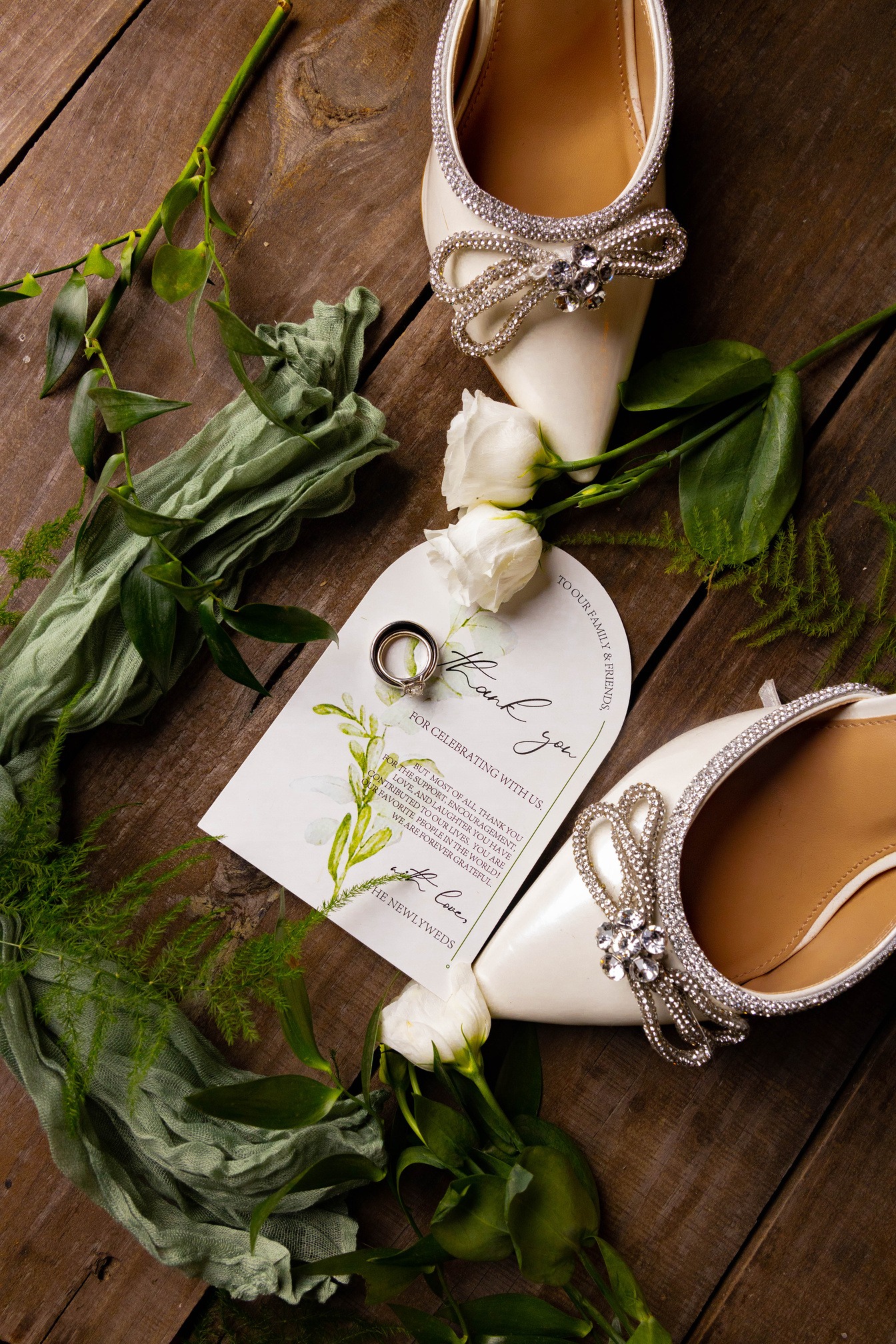 Ring and shoe flat-lay — invitation, band, and floral accents on wood
